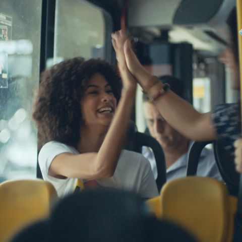 Dentro de um ônibus, duas estudantes se cumprimentam.