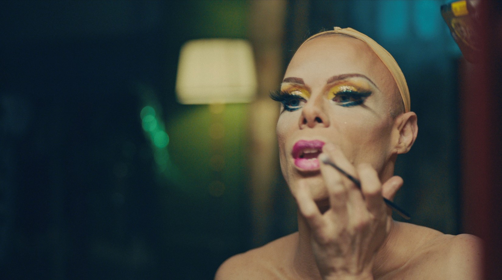Uma drag queen se maquia em frente a um espelho