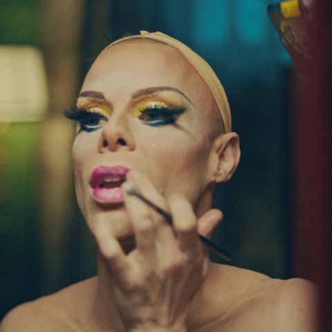 Uma drag queen se maquia em frente a um espelho