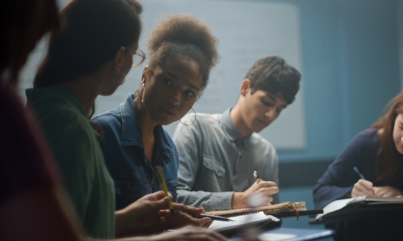 Três estudantes conversam e fazem anotações em seus cadernos