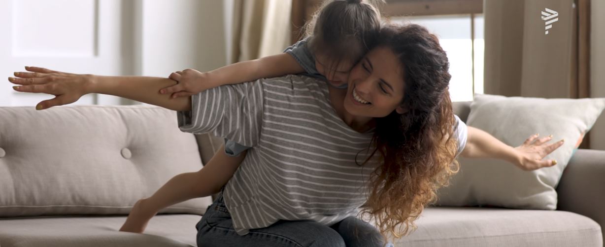 Mãe e filha brincam juntas sorrindo, fazendo o formato de asas com os braços