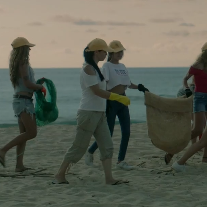 Grupo de pessoas andando na areia da praia, recolhendo lixo