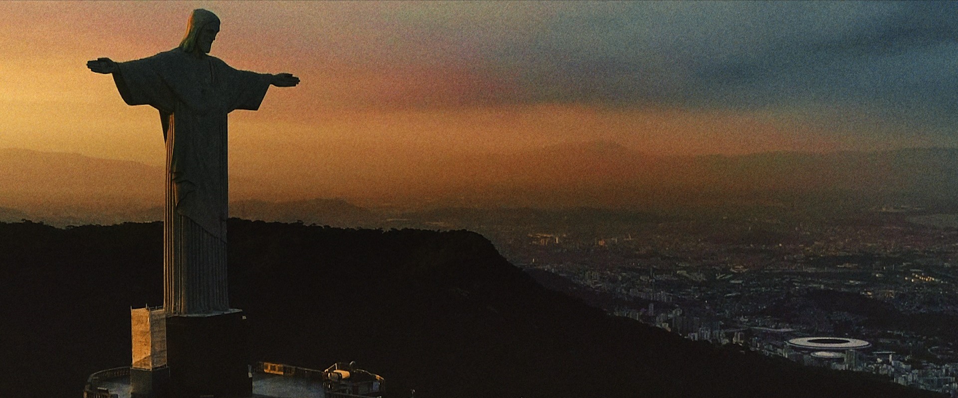 Na imagem, aparece a estátua do Cristo Redentor, e ao fundo o estádio do Maracanã.